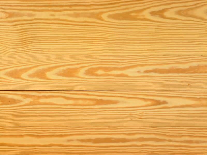 A closeup of yellow pine flooring. The grain is a regular pattern and the color of the wood is a yellowish-brown.