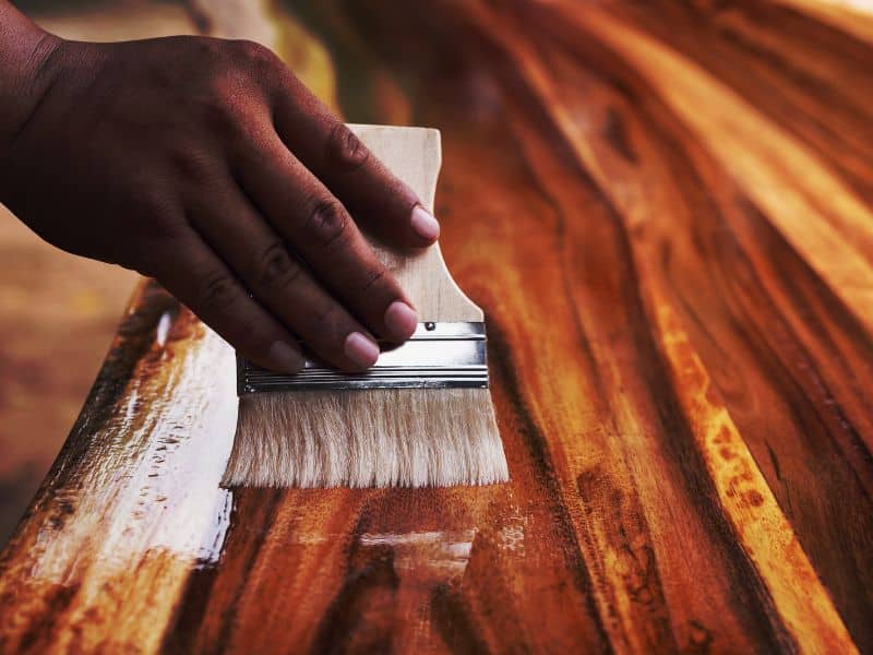 A person applies a top coat to a piece of reclaimed wood using a paintbrush.