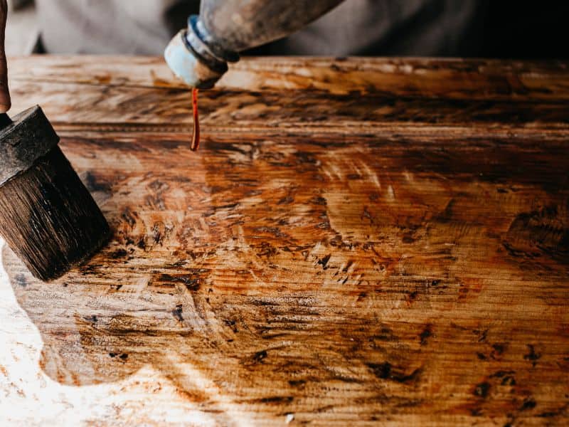 A large brush applies a top coat to a piece of reclaimed wood.