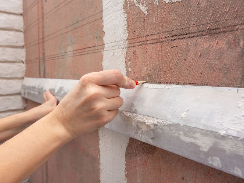 A worker drawing a horizontal line on a wall as a reference point.