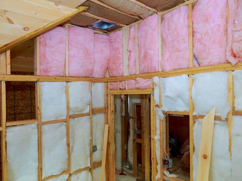 A timber framed house with pink and white fiberglass batts installed between the wall studs.