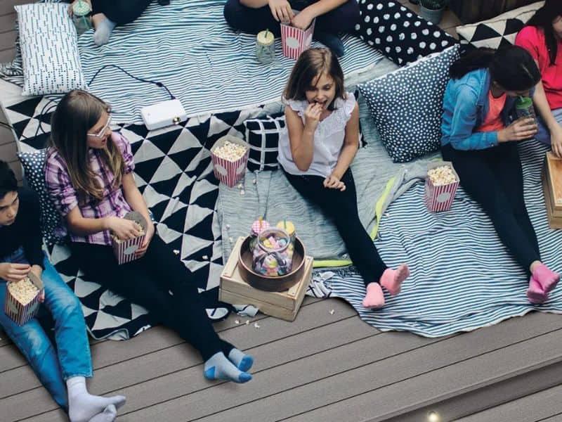 A Fiberon deck with children sitting on cushions and blankets and eating candy and popcorn.