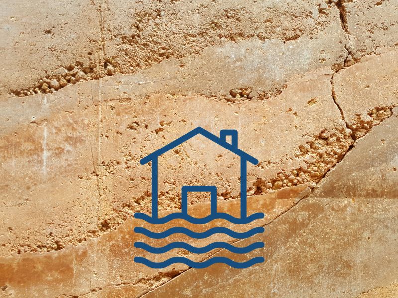 A rammed earth wall with cracks and water damage with a blue house icon with water beneath.