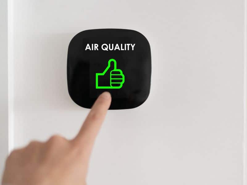 A person's hand presses a black button with their index finger. The button has "air quality" written in white upper case letters and a green "thumbs up" symbol.