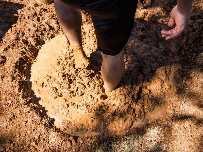 A man mixing adobe mix in a hole in the ground using his feet.