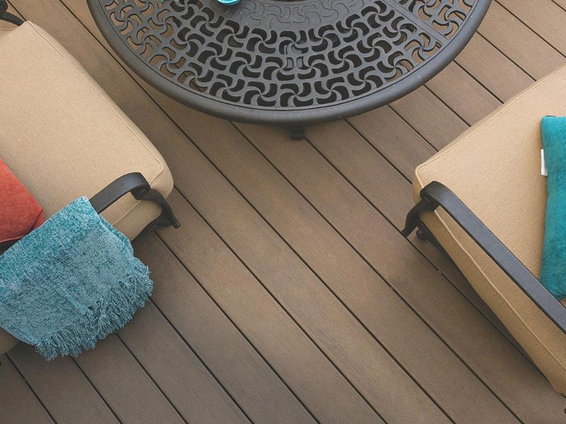 Brown composite decking viewed from above with chairs and a wrought iron table on it.