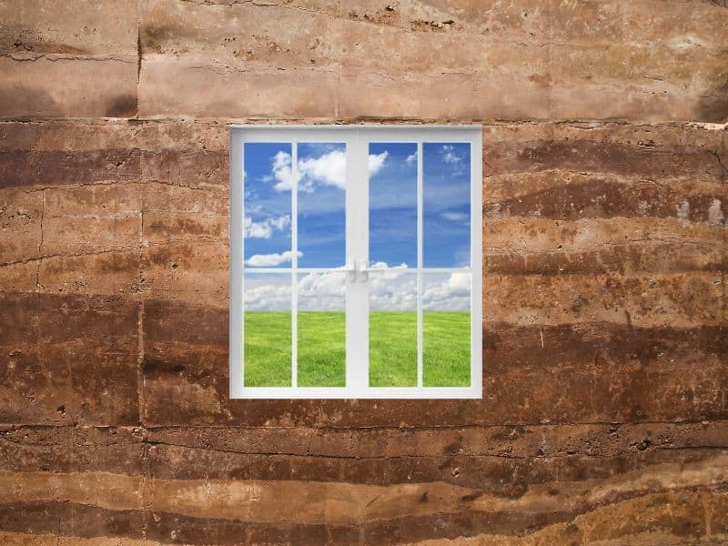 A rammed earth wall with a window showing a view across a field.