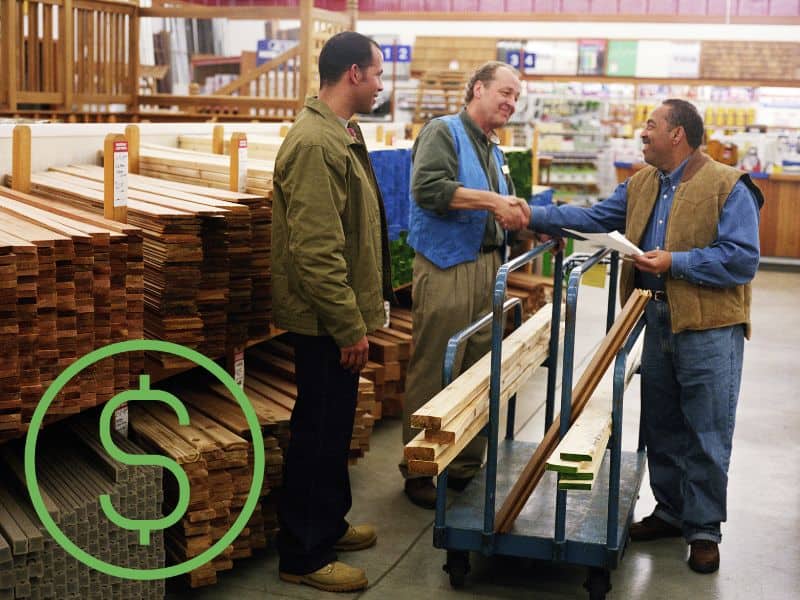 Three men are shaking hands on a deal to purchase timber for use in construction. They are standing inside a store and have battens loaded onto a trolley. There is a dollar sign in the bottom left corner of the image.