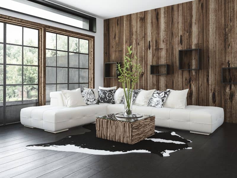 A stylish room with tall windows, a white corner sofa, and reclaimed wood coffee table, and a matching reclaimed wood accent wall behind.