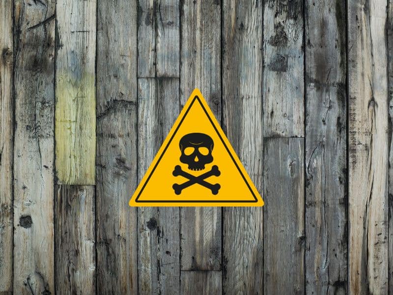 A reclaimed wood wall with a triangular yellow warning sign with a black skull and crossbones on it.