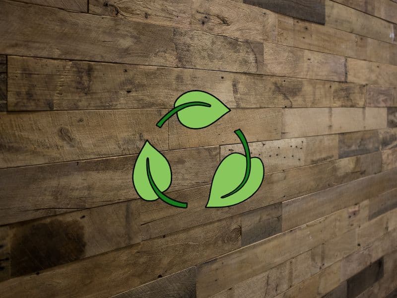 A wall made from reclaimed wood planks. Overlain are three leaves arranged in a circular patter to indicate sustainability.