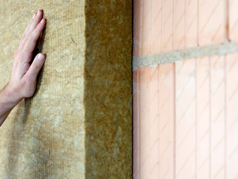 A mineral wool batt is being installed against a red brick wall.