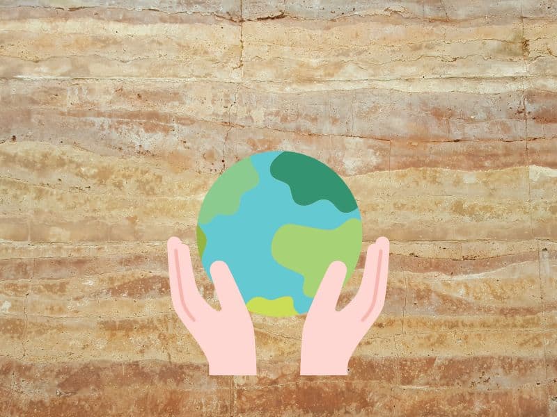 A photograph of a rammed earth wall with a drawing of planet earth held in two hands to indicate sustainability.