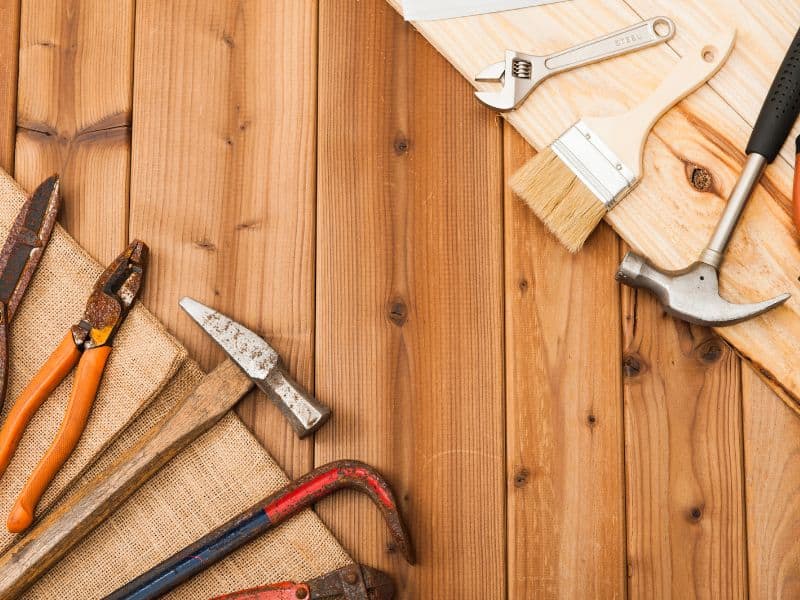 An assortment of tools is laid out on reclaimed wood planks. They include hammers, pliers, and a paintbrush.