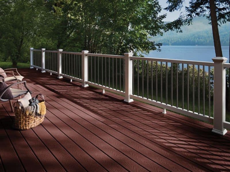 A large decked area overlooking a lake. The deck has white railings around its edge and trees and grass can be seen through the railings.