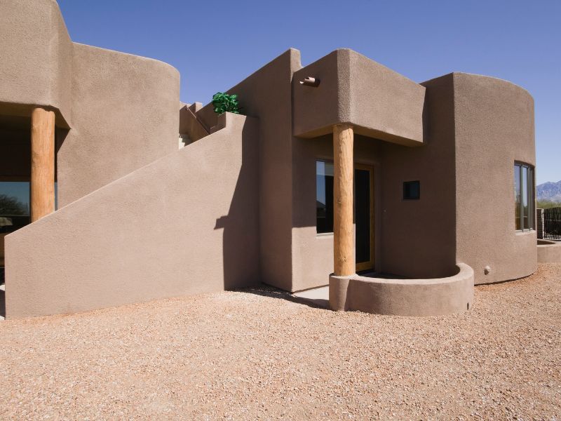 An adobe building with smooth rendered walls. It has a brown, rusty appearance and modern stylish windows.