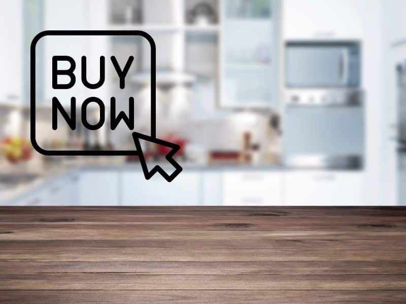 A reclaimed wood countertop with a blurred kitchen in the background. In the upper left is a button with a mouse pointer hovering over it containing the text "buy now."