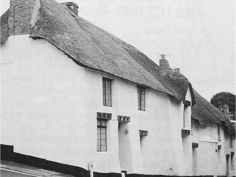 A photograph of a historic building built out of cob in the 16th Century in England. The photograph is black and white and shows a thatched roof on top of the cob walls.