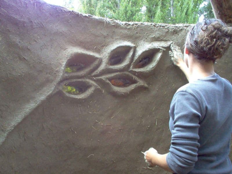 A woman puts the finishing touches on a cob wall with beautiful embellishments in the shape of leaves. 