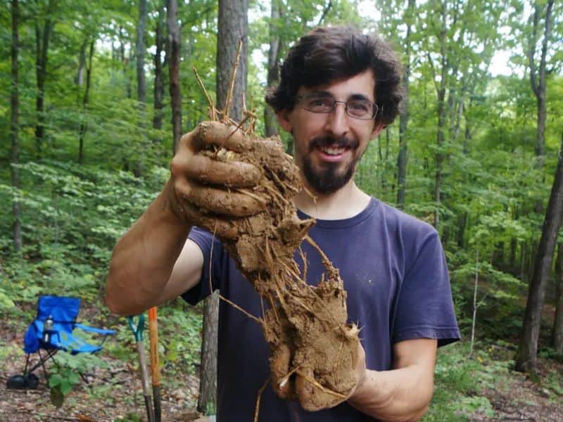 A man holding some cob mixture shows it to the camera. There are trees in the background.