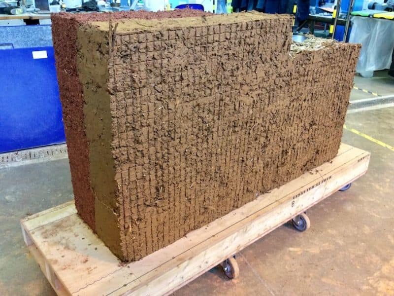 A photograph of a section of cob wall built in the laboratory comprises two layers: a stronger, denser layer for structural strength and a less dense layer with better thermal insulation. The section of wall sits on a pallet with wheels.