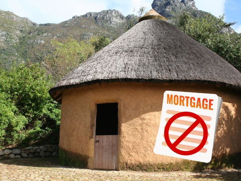 A round cob house with a thatched roof and stable door. Behind the house are mountains and trees. In the lower right corner is a cartoon mortgage document with a red circle with a line through it to show it has been declined.