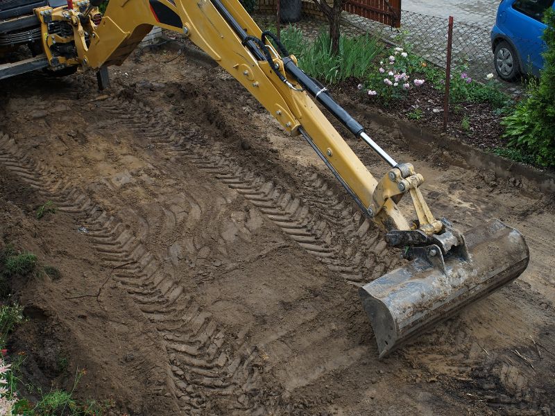 A yellow excavator using its backhoe to level a building site.