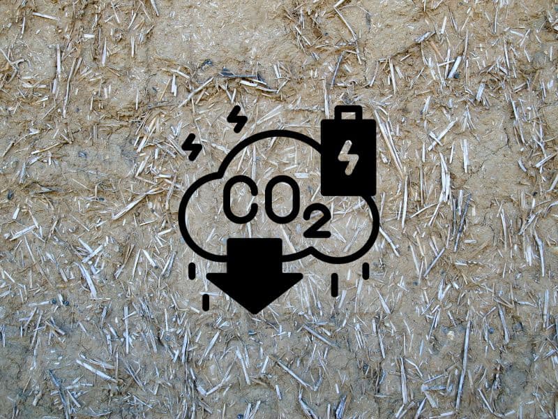 A closeup of a cob wall showing pieces of straw on its surface. Overlain is an icon of a cloud labeled with "CO2" and a downward-pointing arrow and battery alongside to indicate low CO2 emissions and low embodied energy.