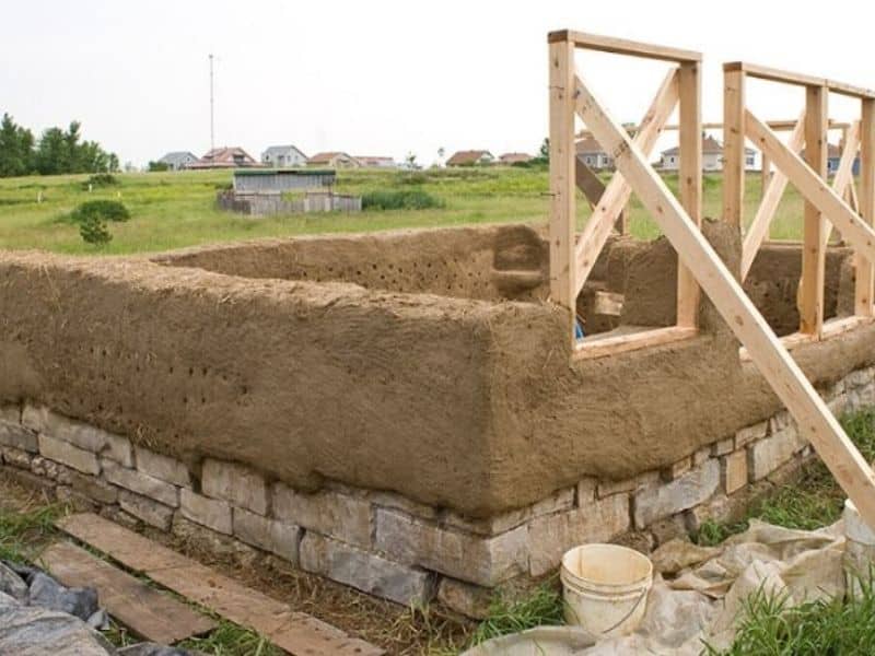 Cob house foundations made from stone with the first layer of cob laid and timber window frames.