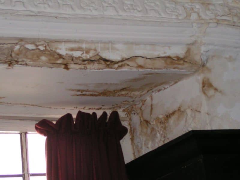 A photograph showing water damage to interior plasterwork in a cob house. Brown staining and cracks have appeared in the surface of the internal wall.