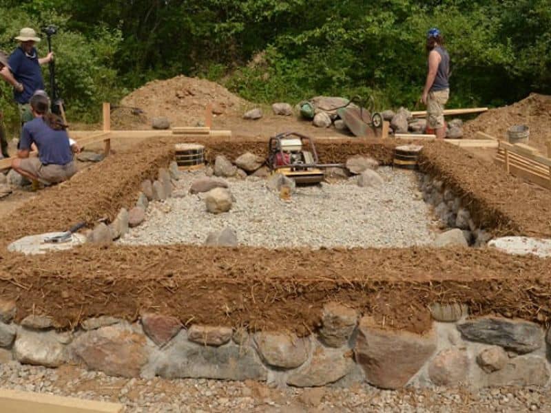 Stem walls for cob house foundations constructed from stone. The first layer of cob has been placed on top of the stem wall.