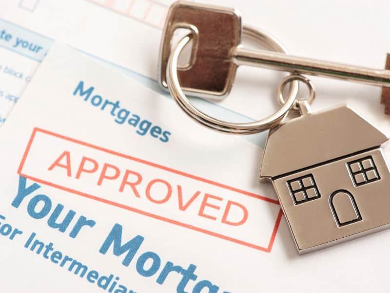 Mortgage approval paperwork has an "approved" stamp, a house key lying on top, and a key fob with a house attached.