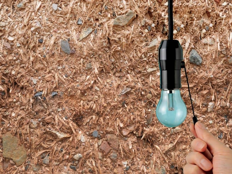 A cob wall with a light hanging down and a person's hand switching it on at the cord.