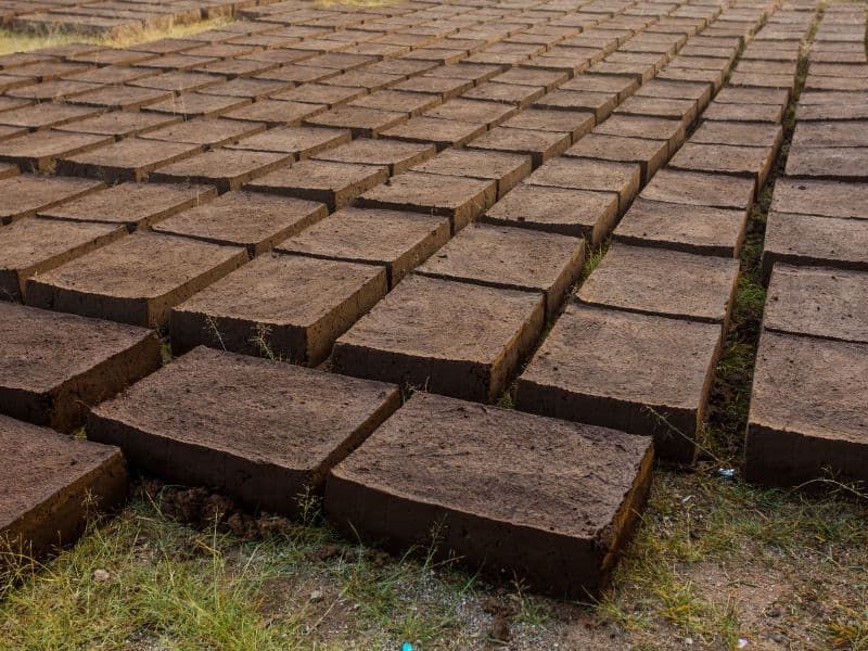 Adobe bricks are set out in neat rows to dry on flat rough ground.