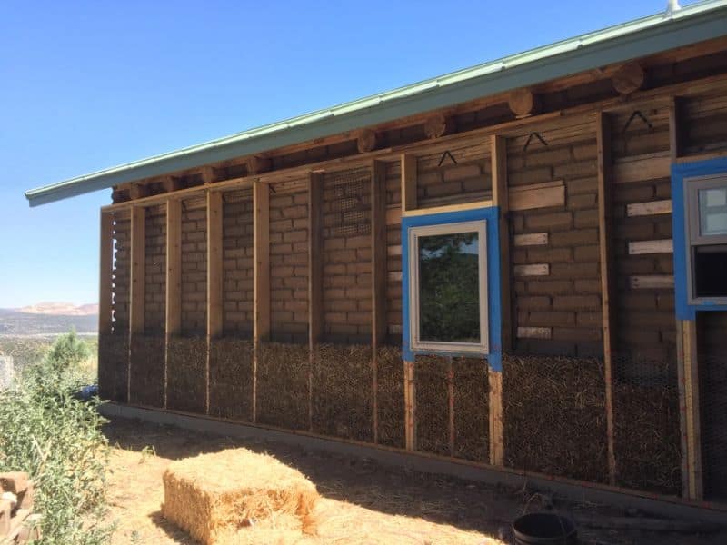 An adobe house with an outer wall comprising a straw-clay mix held in place by chicken wire. The chicken wire is stapled to wooden battens fastened to the adobe brick wall.