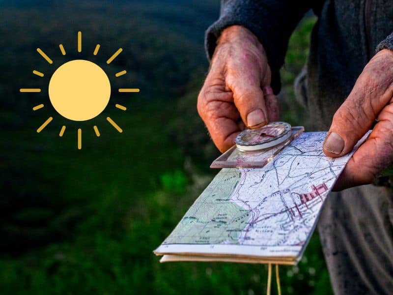 A photograph of a man's hands holding a map with a compass laid on it. In the left upper corner is a sun icon.