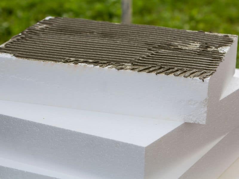 Blocks of rigid polyurethane insulation stacked in a pile with adhesive spread on the top of the uppermost block ready for application to an adobe wall.