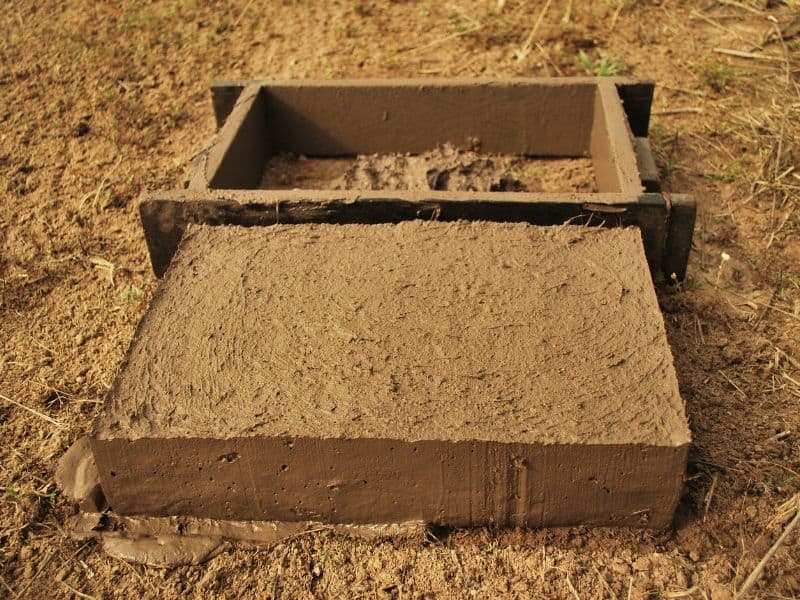 An adobe brick has just been taken out of the wooden form used to mold it into shape.