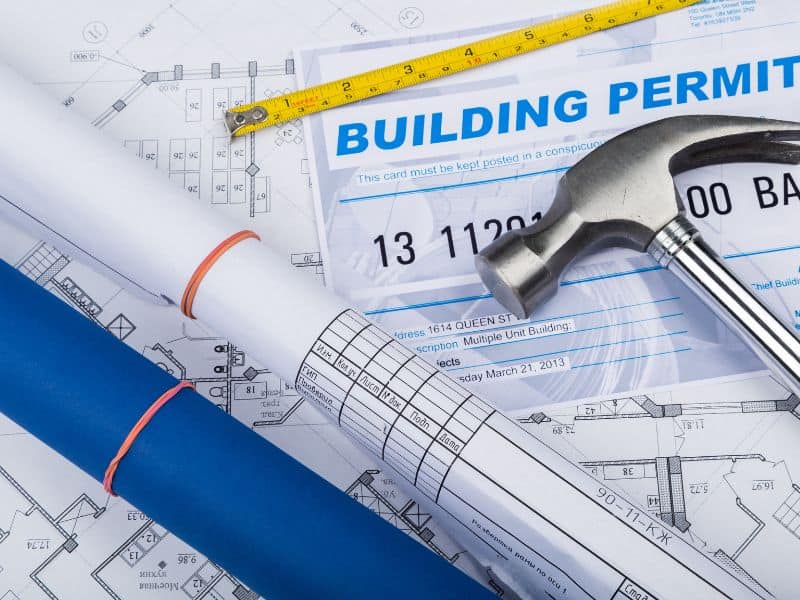 A set of building permits laid out on a desk with a hammer and tape measure on top.