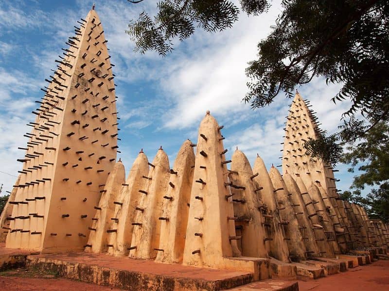 The Grand Mosque of Bobo-Dioulasso. It is made from adobe and has many wooden posts protruding from tall spires.