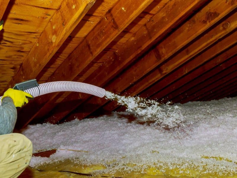 Loose-fill insulation is blown into a roofspace using a hose.