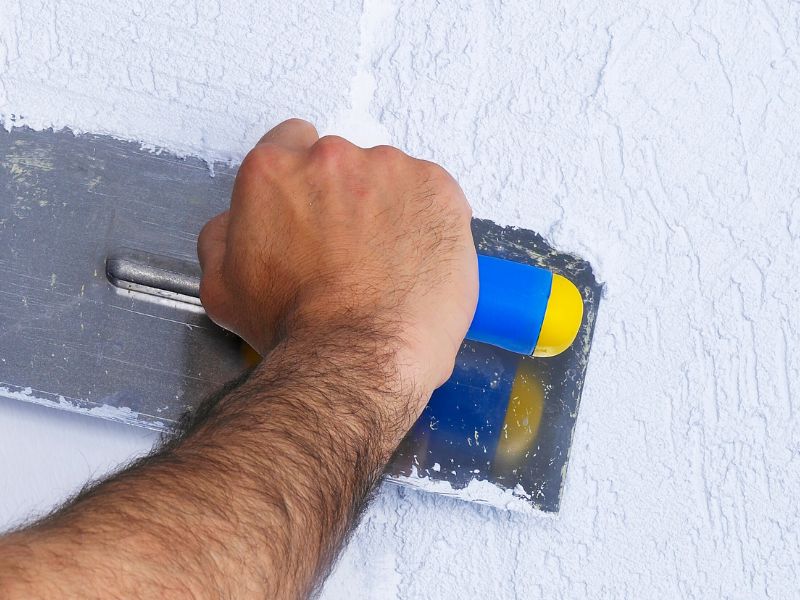 A man's hand working lime plaster with a metal float.