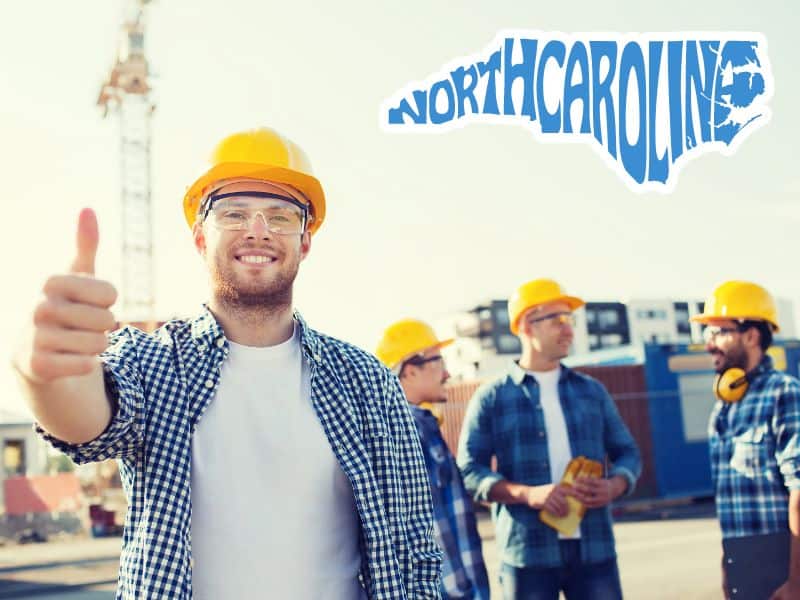 A smiling builder wearing a blue and white plaid shirt, safety glasses, and a yellow hard hat with his thumb up. In the background are other builders, similarly dressed on a building site. In the top left corner of the image is an outline of the state of North Carolina with the words "North Carolina" in blue and shaped to fill the outline of the state.