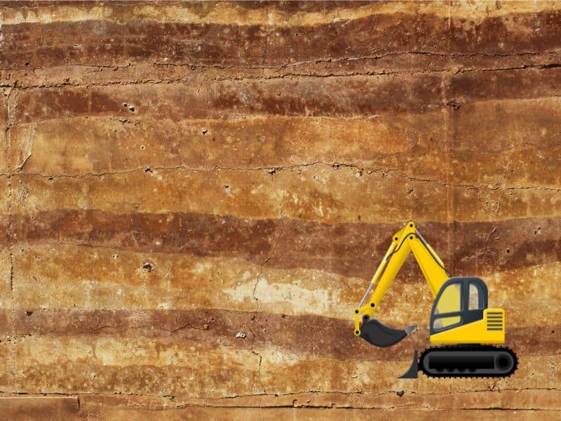 A photograph of a rammed earth wall with the individual layers visible in different shades of brown. On the lower right-hand side, is a yellow cartoon digger.