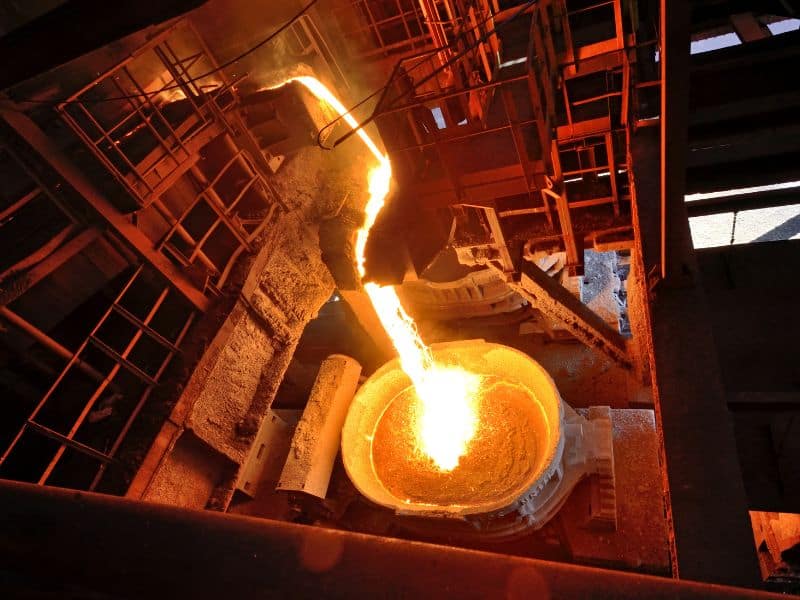 A steel furnace with molten steel pouring from it into a crucible in a steelworks.