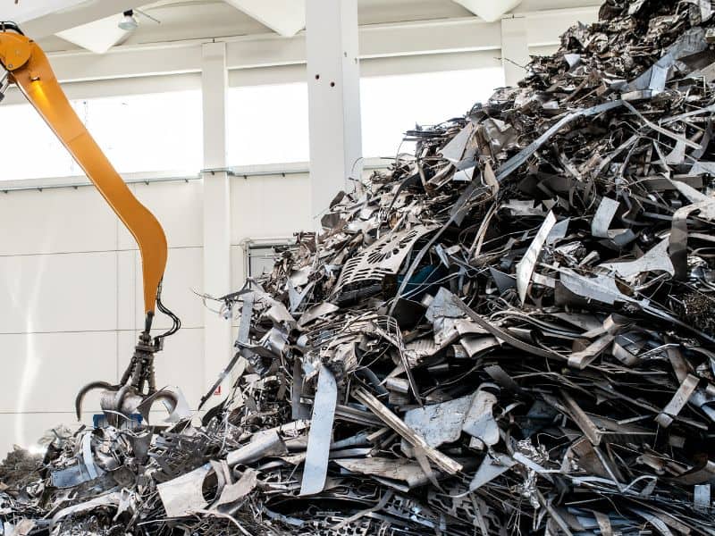 A yellow-armed mechanical grab handling scrap steel inside a warehouse.