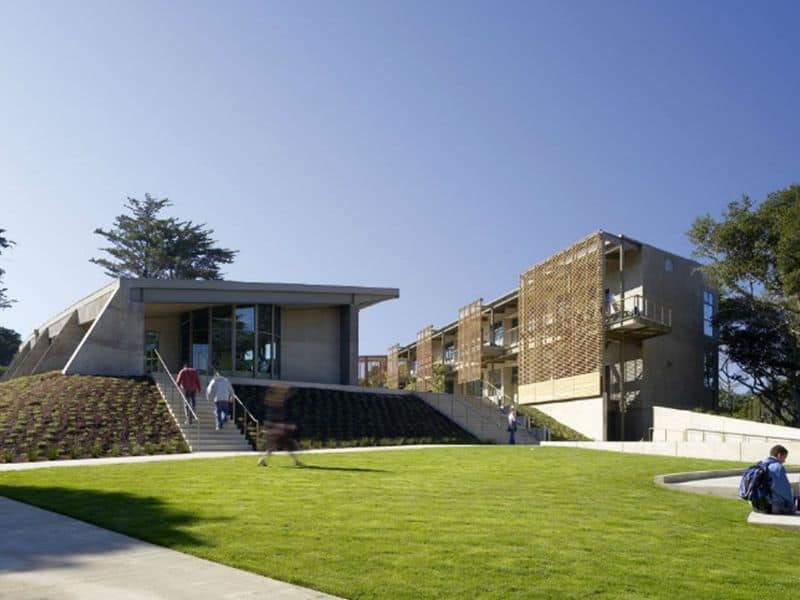 The Nueva School with steps rising from a grassed area to a paved square with buildings on either side that have green roofs.