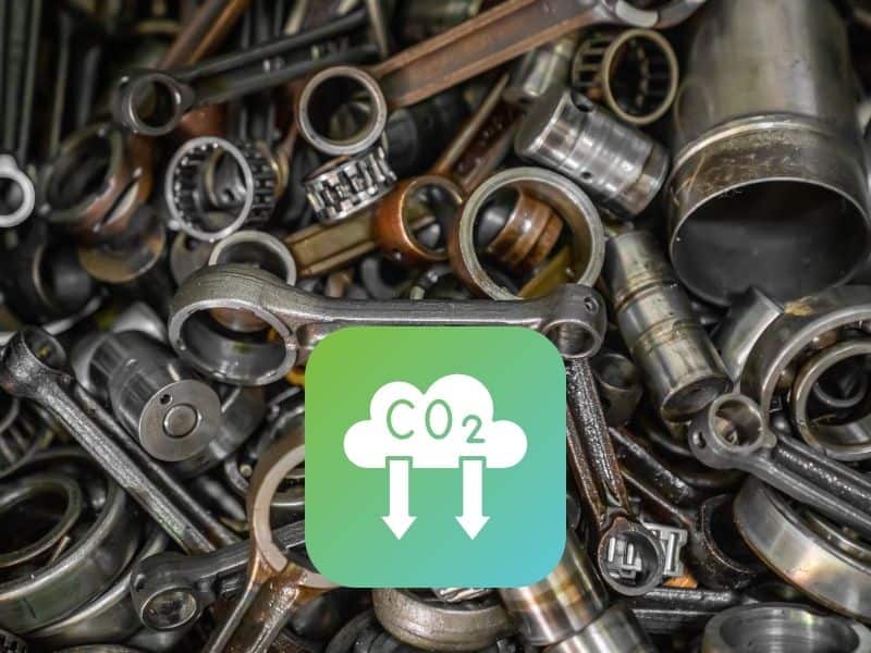 Assorted steel scrap with a green graphic with a cloud of CO2 and arrows pointing downward.