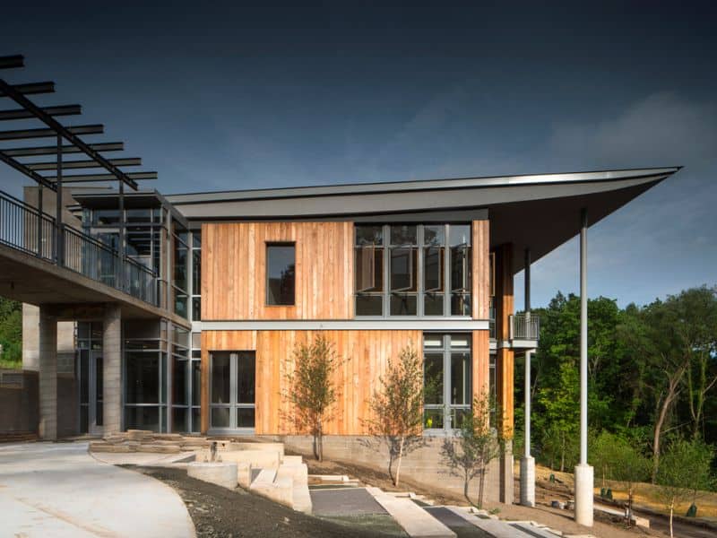 A photograph of the Frick Environmental Center, a wooden-clad, steel-framed building built on a slope next to woodland.