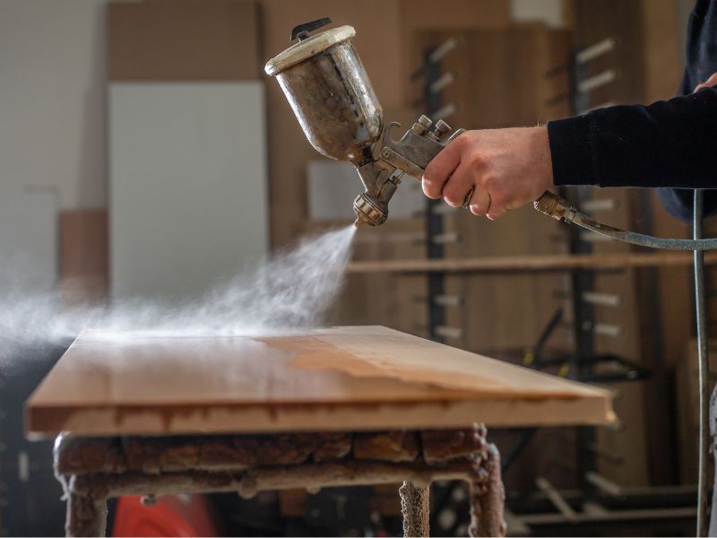 A sealant is sprayed onto a sheet of reclaimed wood.